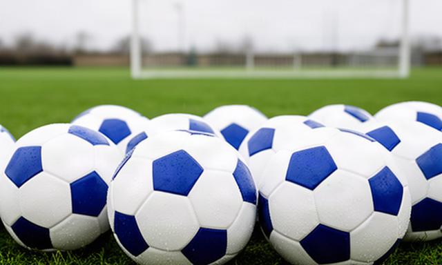 Witte en blauwe voetballen op een groen voetbalveld met doel op de achtergrond