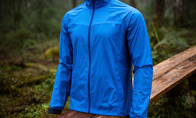 Lichtgewicht blauw hardloopjack op een houten bankje naast een bosrand